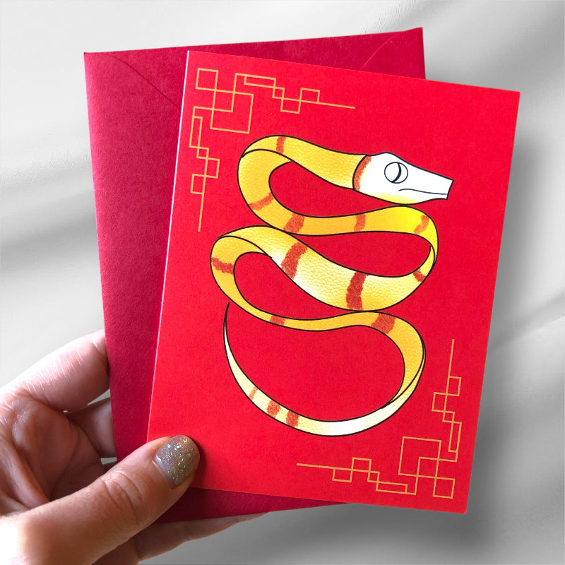 lunar new year card with yellow snake, and red envelope in hand, against a white backdrop