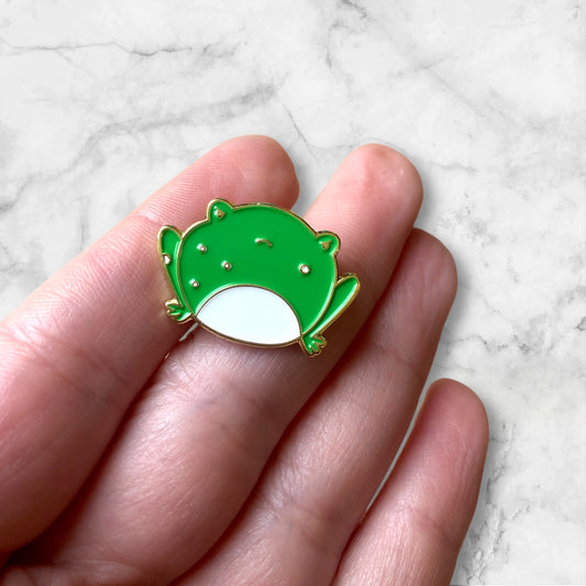 angry but cute frog pin in hand, against a marble background