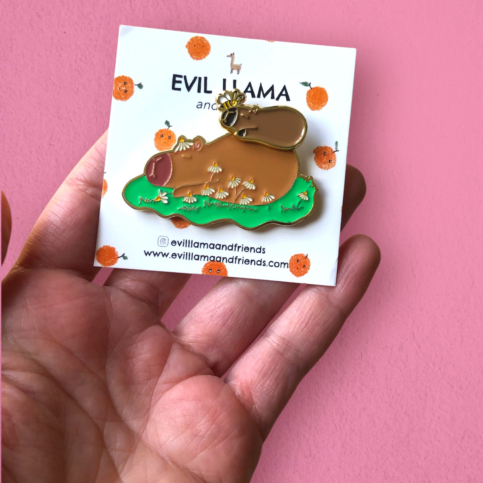 capybara pin with magnetic feature on backing card, in hand, against a pink background
