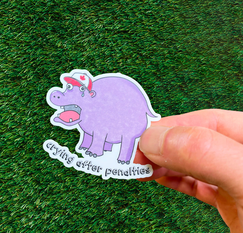 sticker of a crying hippo wearing a Team Canada ball cap with a red maple leaf, against a grassy background