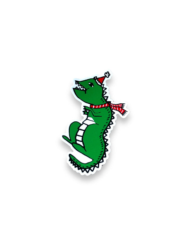 festive dino vinyl sticker. the cartoon t-rex is wearing a santa hat and a red scarf with white stripes