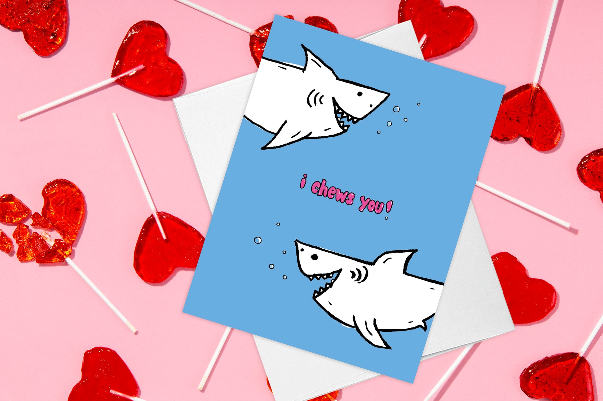 i chews you sharks love card styled against a fun pink background with candy hearts, some with bites taken out of them.