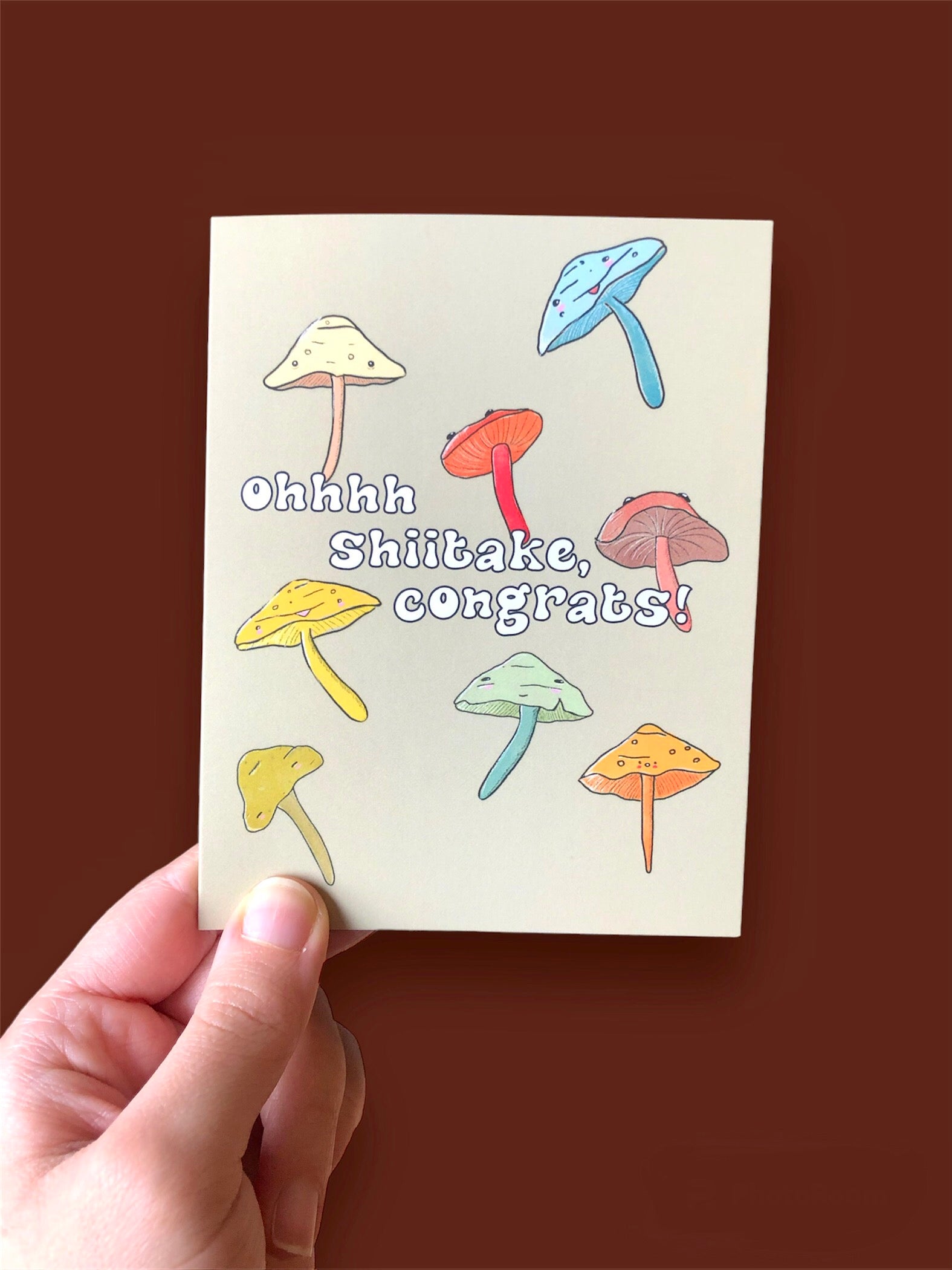 punny congratulations card, showing several shiitake mushrooms, in hand, held against a brown background