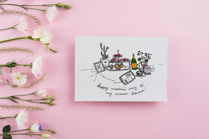 cute mothers's day card showing an elegant brunch scene with high tea, caption reads "happy mother's day to my mama llama". the card is styled against a pink background with white flowers