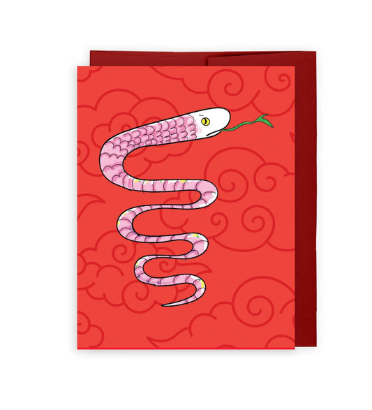 lunar new year card featuring a cute, pink cartoon snake against a red background with dark red cloud motif. the card sits on top of a matching red envelope