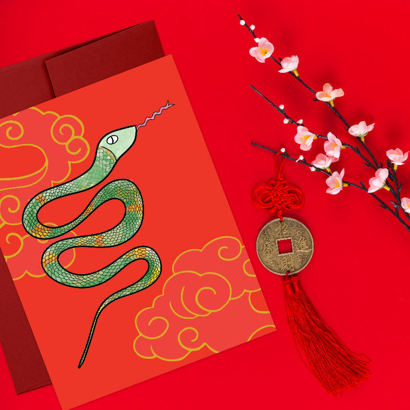 lunar new year card with green snake styled against a red background, with red envelope, pink cherry blossoms, and old good fortune coin