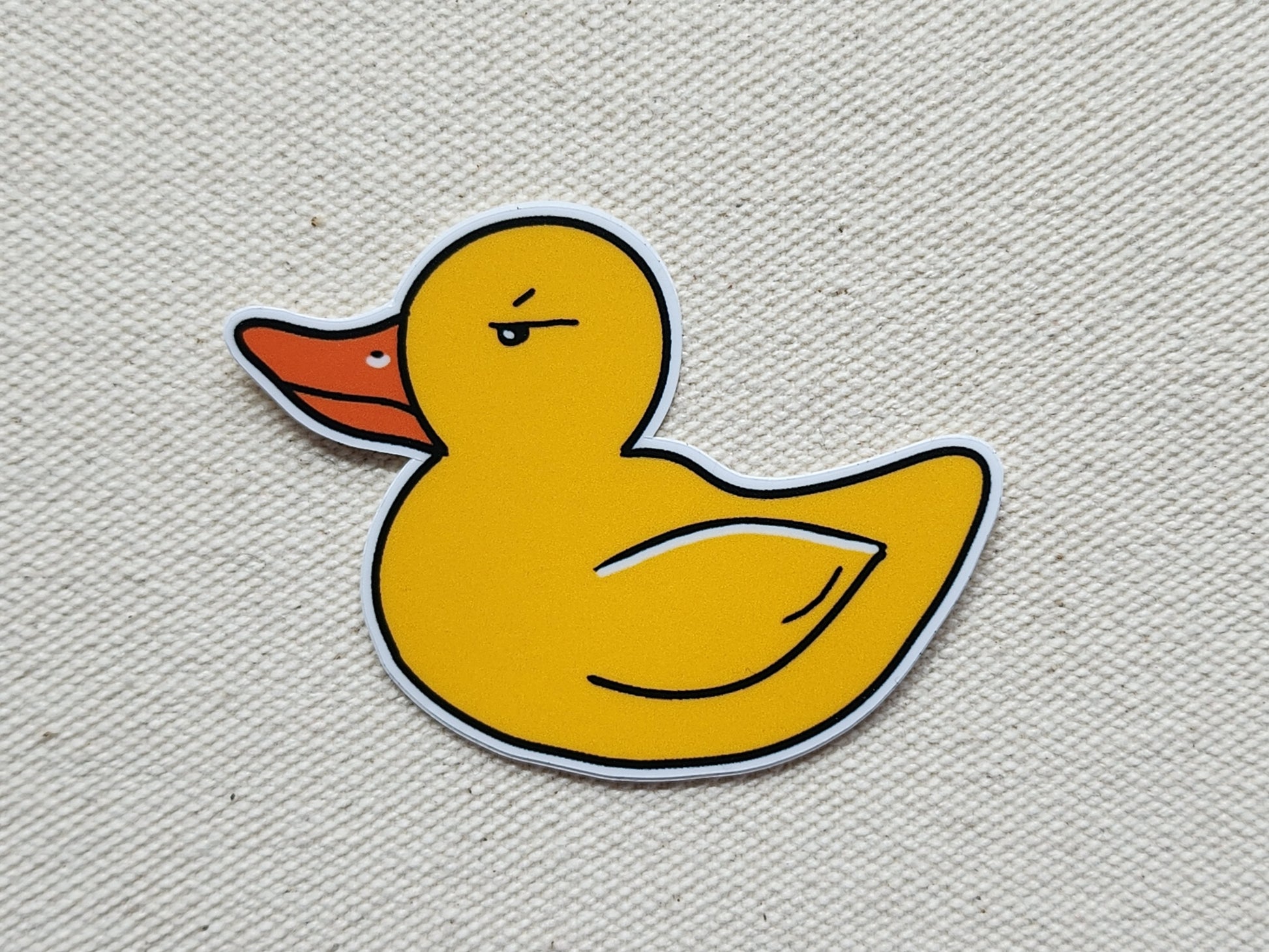 Yellow rubber duck sticker on a textured beige background