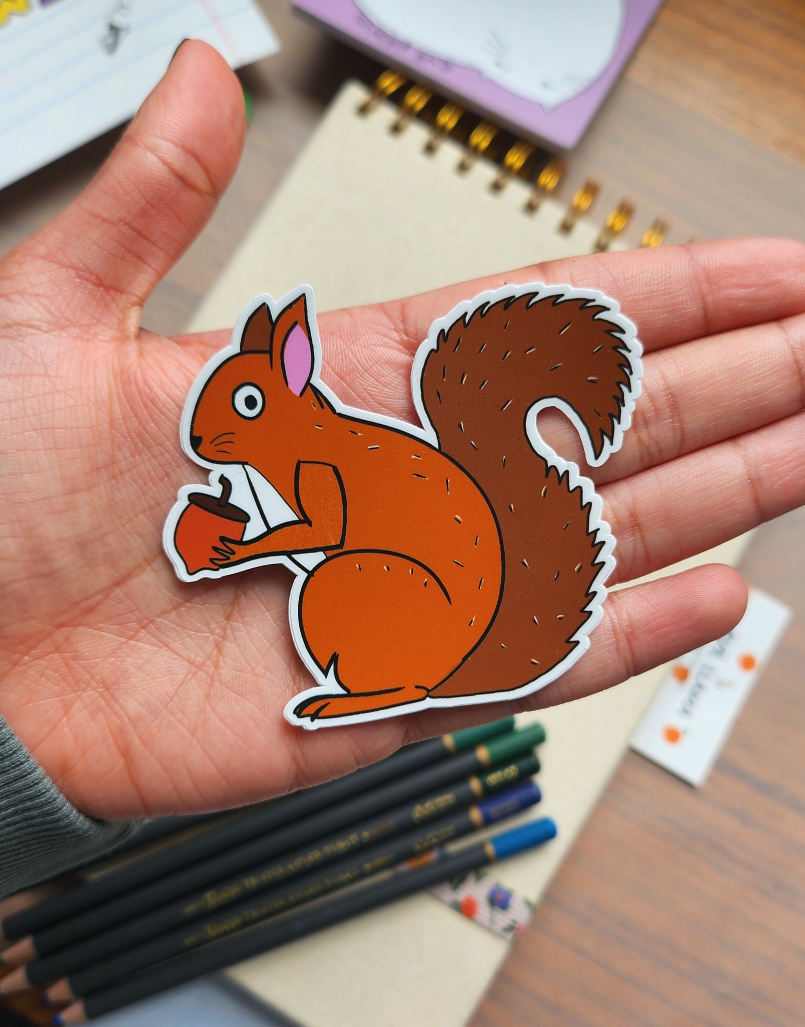Hand holding a squirrel sticker with stationery items in the background