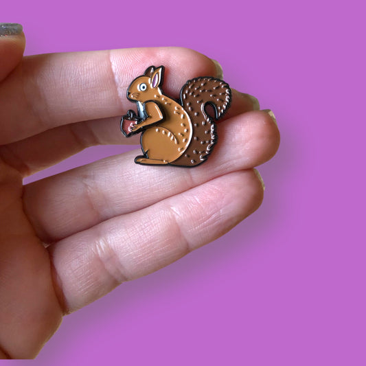 little squirrel enamel pin in hand, against purple background