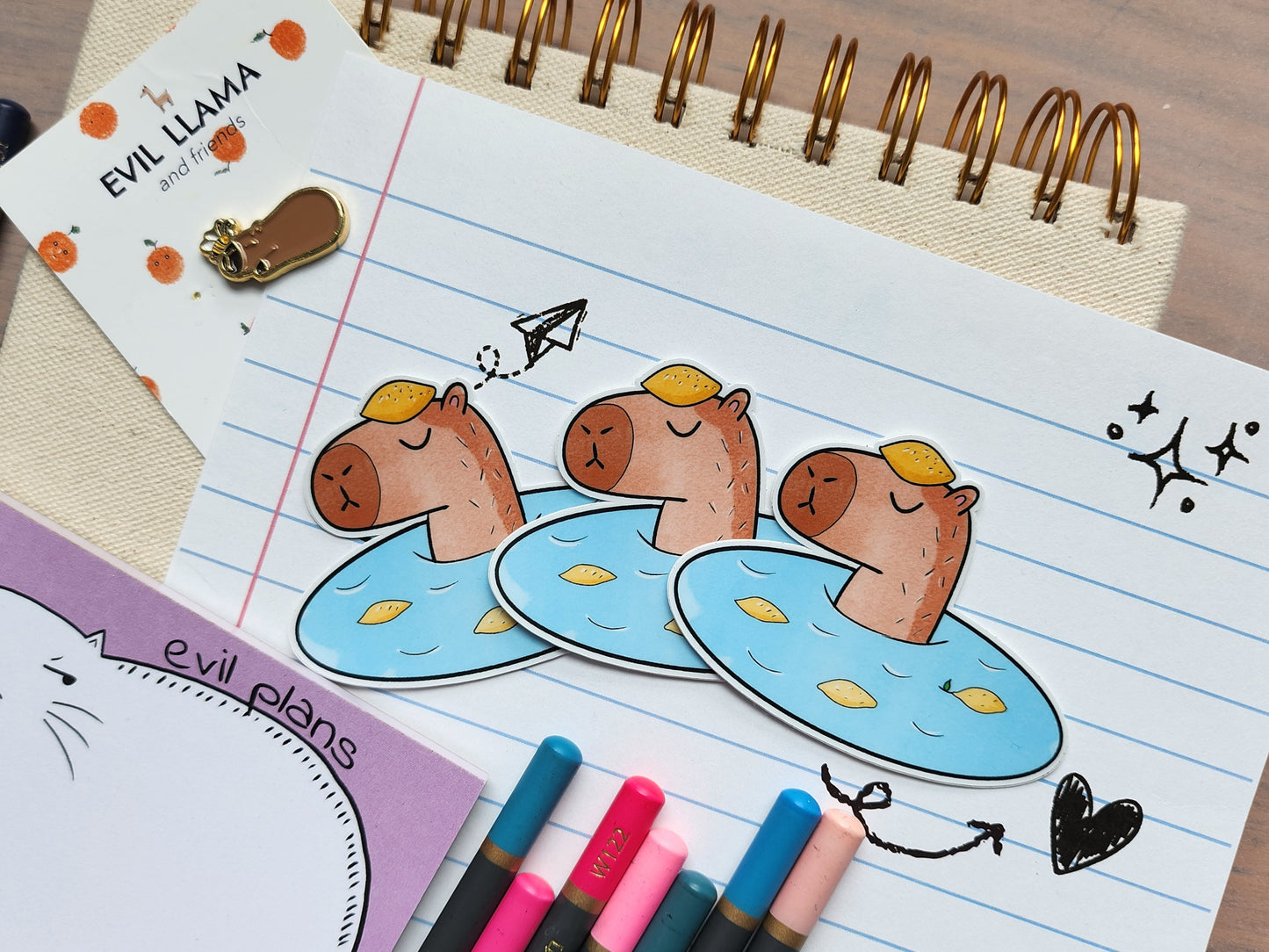 3 capybara in onsen stickers on a lined notebook, styled with some coloured pencils and other stationery