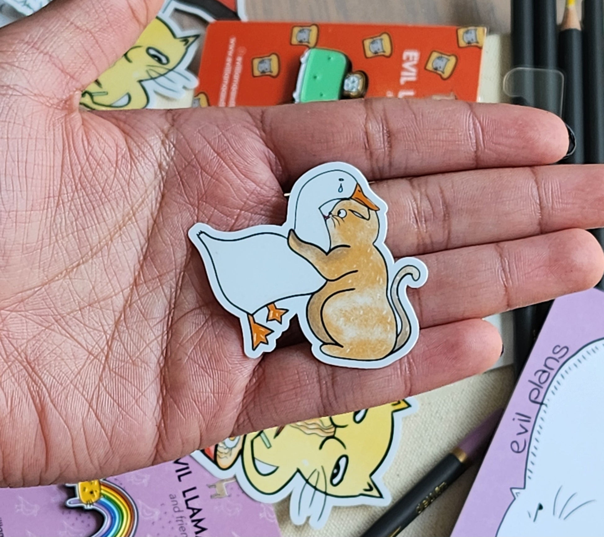 Hand holding a sticker of a cat and duck, surrounded by other stickers and stationery items.