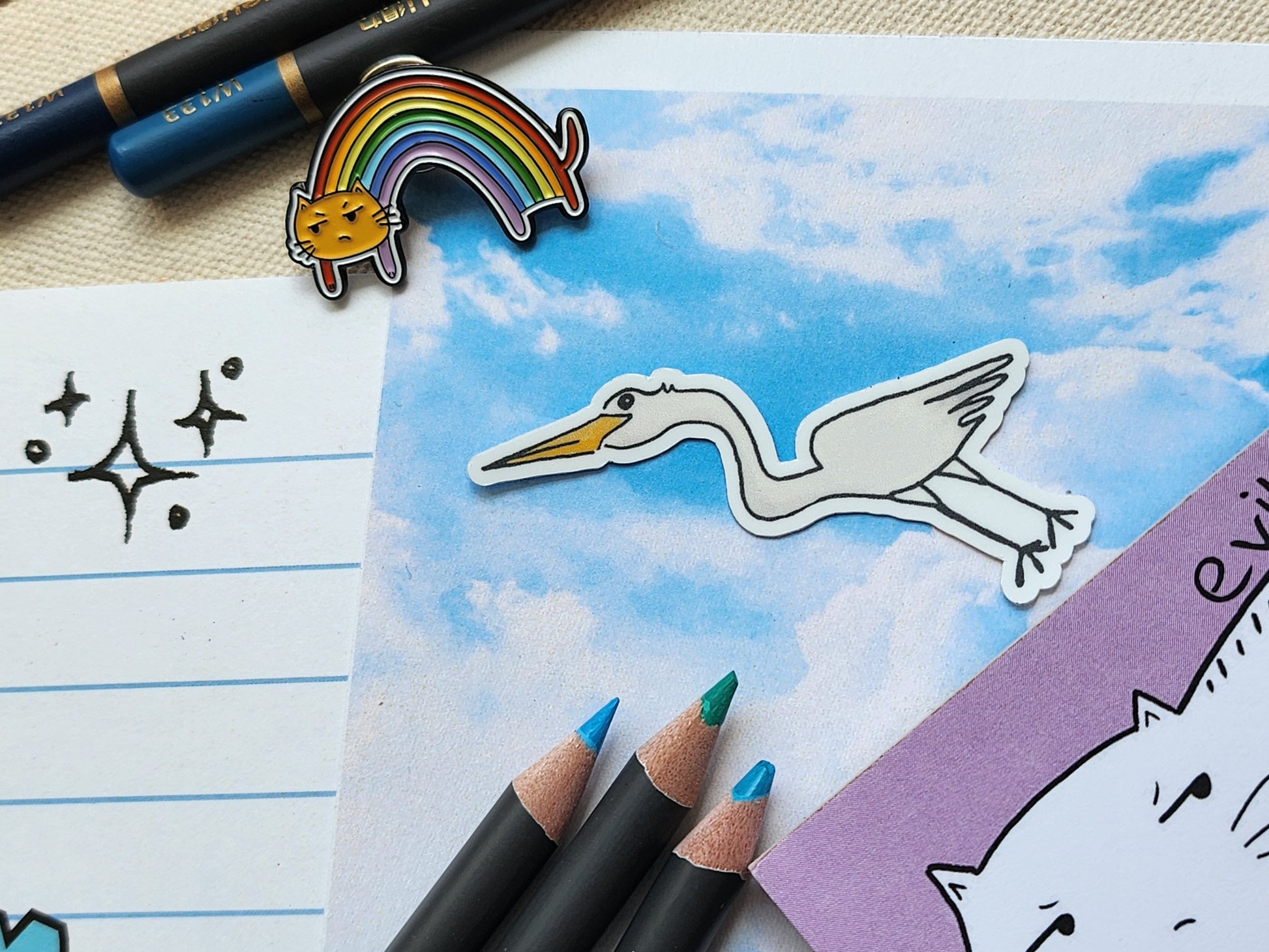 egret sticker on a blue sky illustrated paper, surrounded by colouring pencils and other stationery items