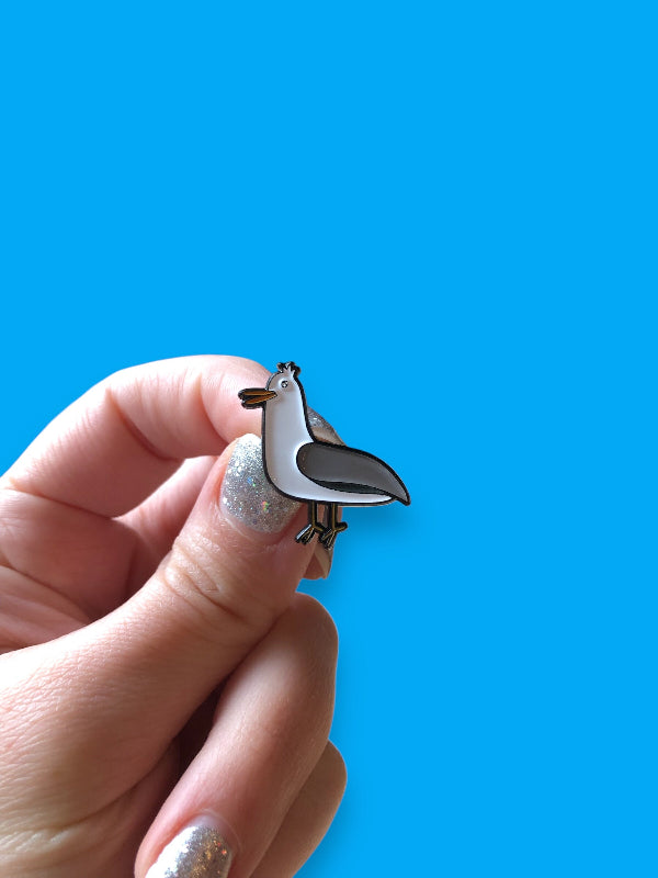 gus the gull enamel pin in hand to show scale, against a light blue background