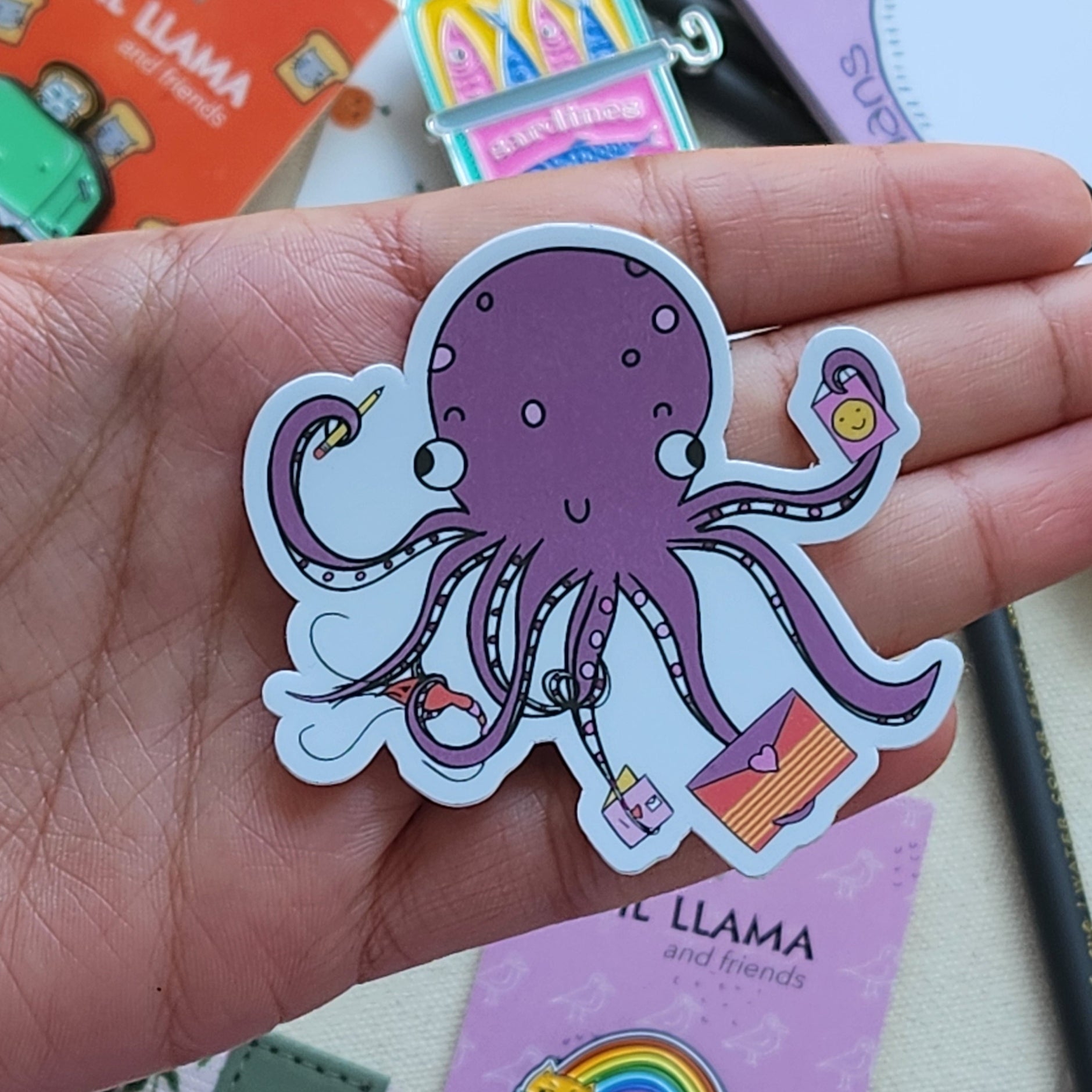 Hand holding a happy octopus sticker surrounded by stationery items.