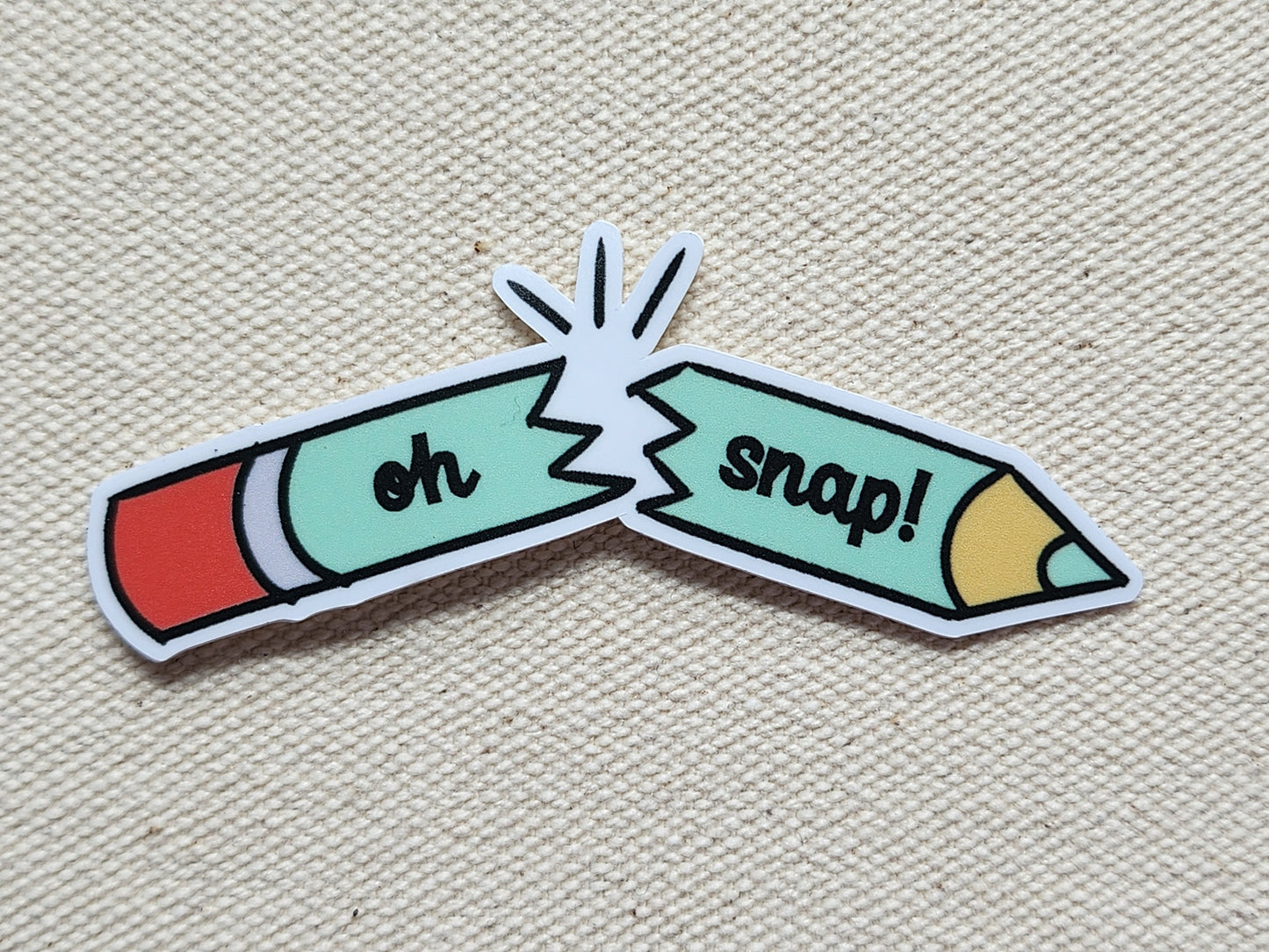sticker of a broken pencil with the text reading "oh snap!", on a textured, beige background