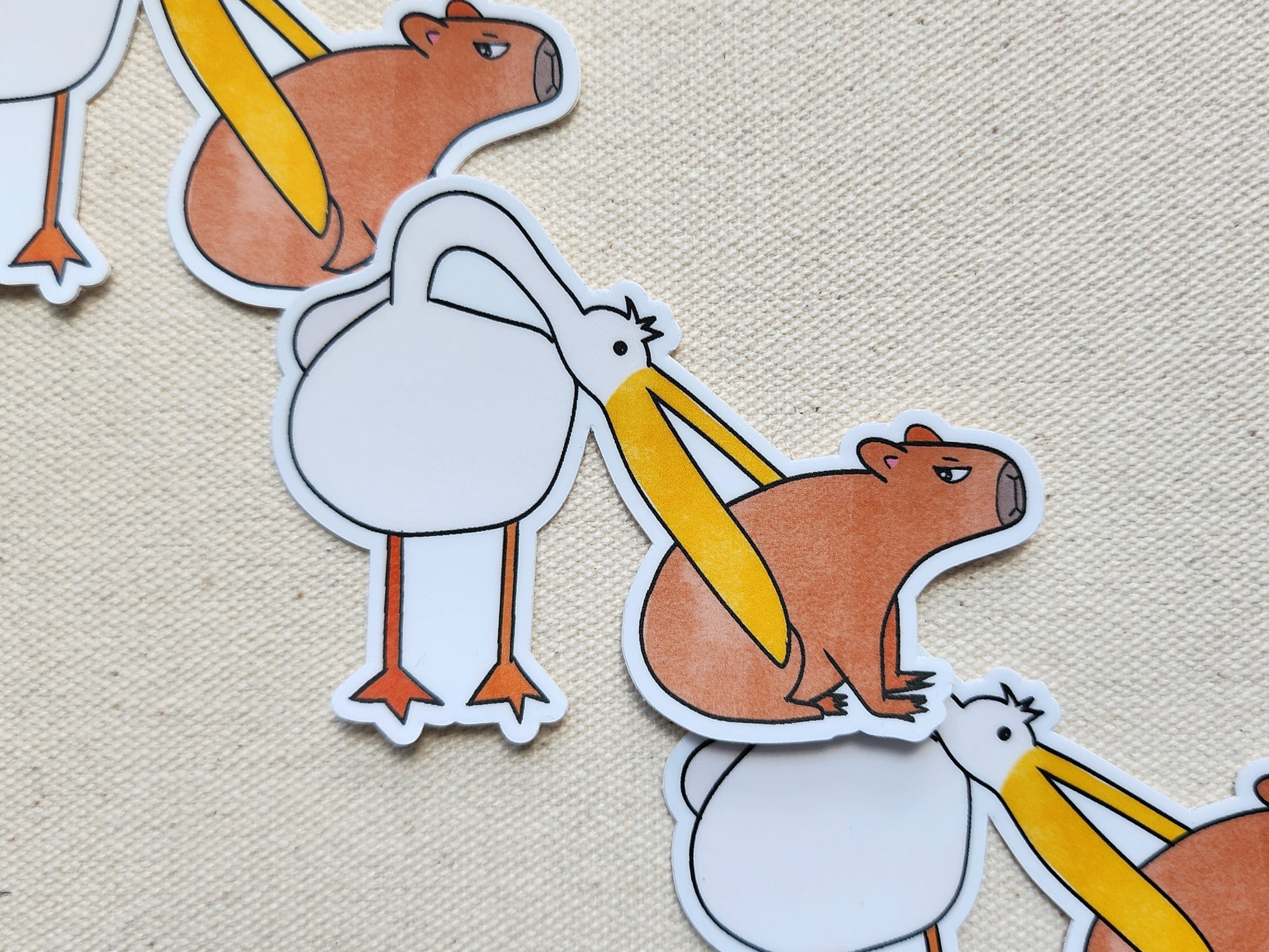 3 "pelican eats capybara" stickers styled on a beige, textured background