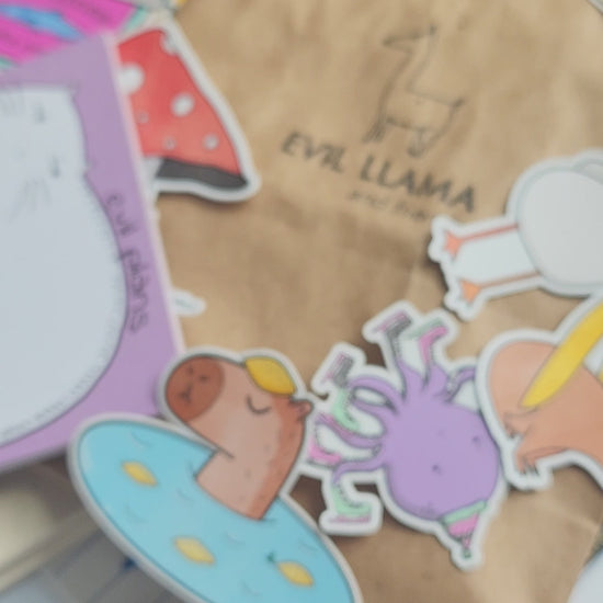 hand holding a "seal of disapproval" enamel pin, with stickers and various stationery items in the background