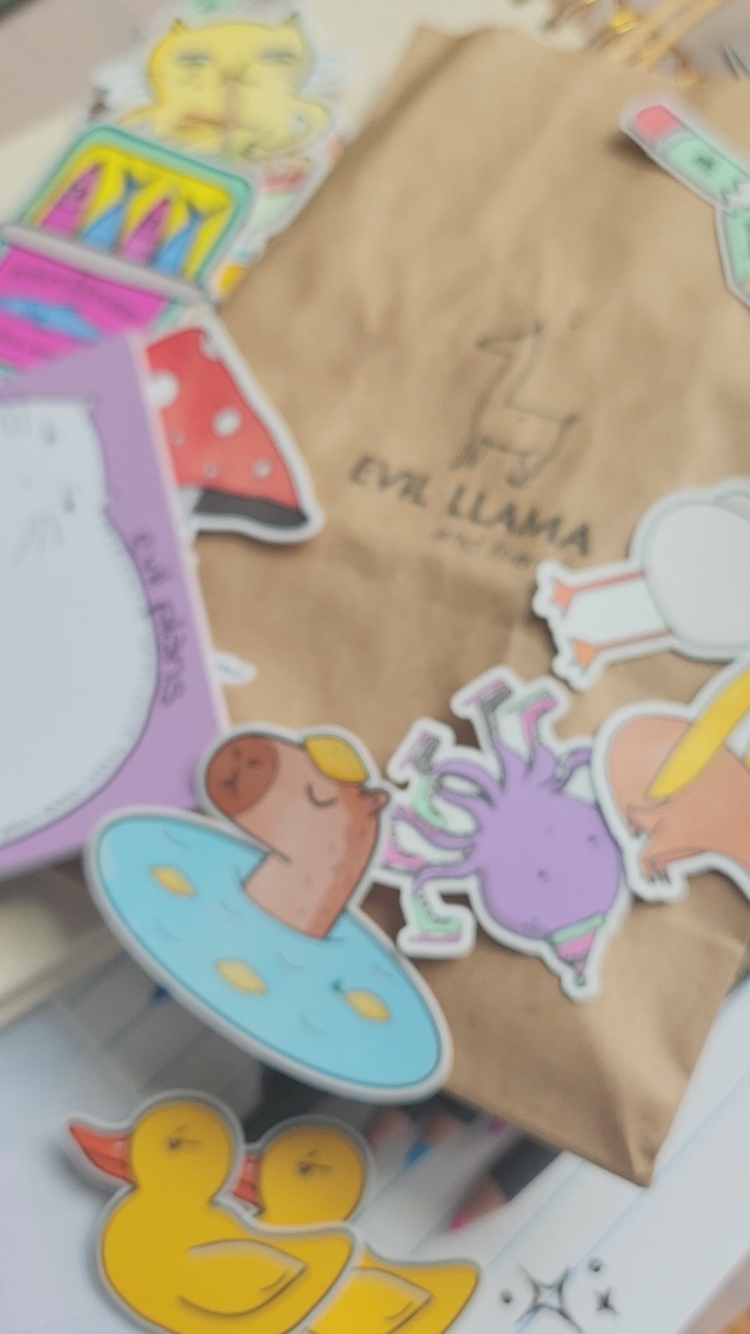 hand holding a "seal of disapproval" enamel pin, with stickers and various stationery items in the background