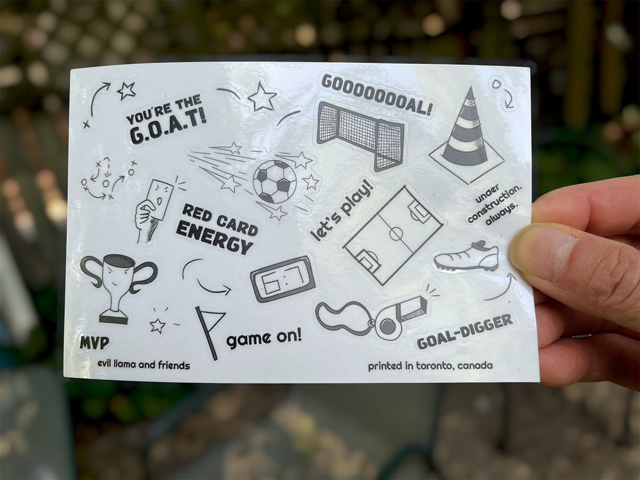 Hand holding a sticker sheet of black and white sports elements with text and graphics.