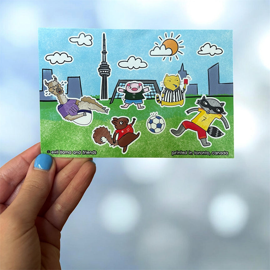 sticker sheet portraying cartoon animals playing soccer with the CN tower in the background, held by a hand.
