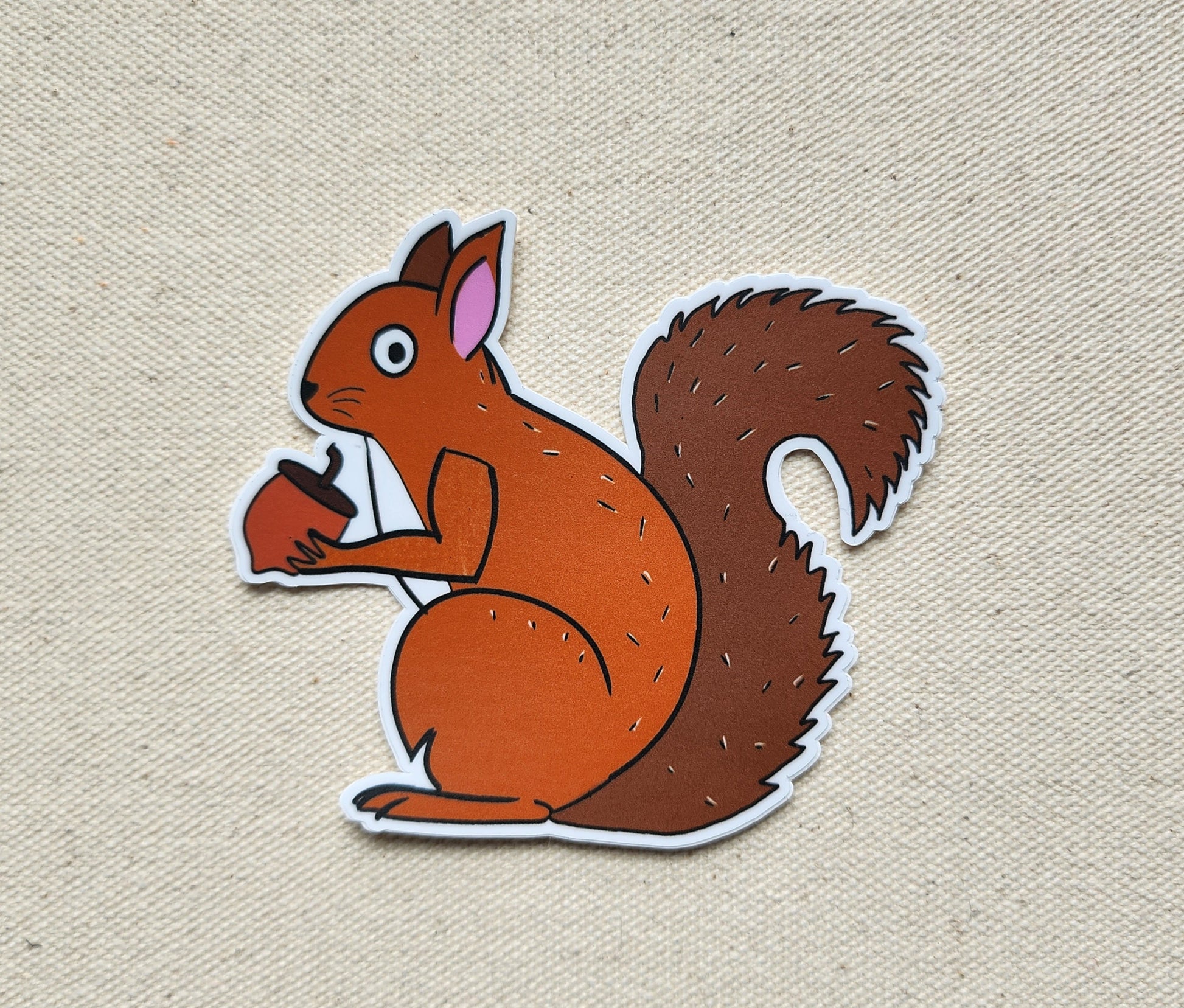 sticker of a cartoon squirrel holding a nut on a beige background